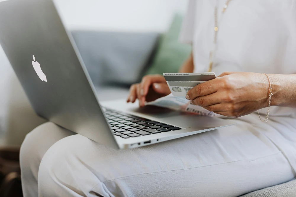 Person shopping online using a MacBook and holding a credit card, representing secure e-commerce or digital payment on a modern website.