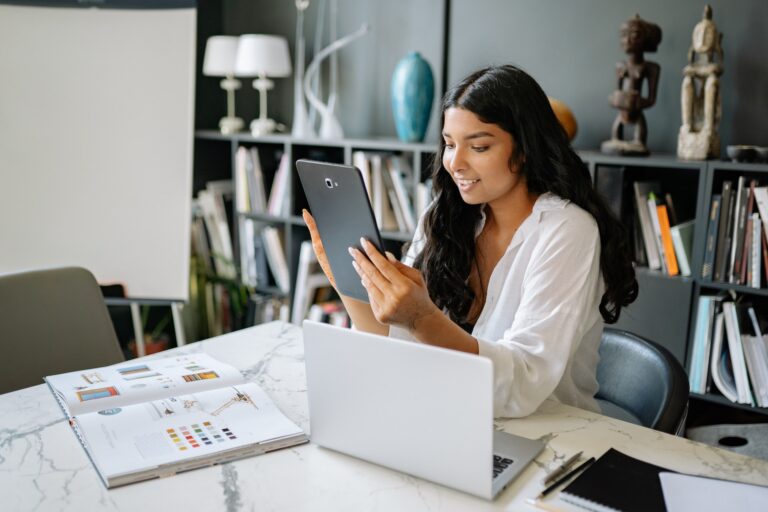 Young woman seated a desk looking at a smart tablet in her hands