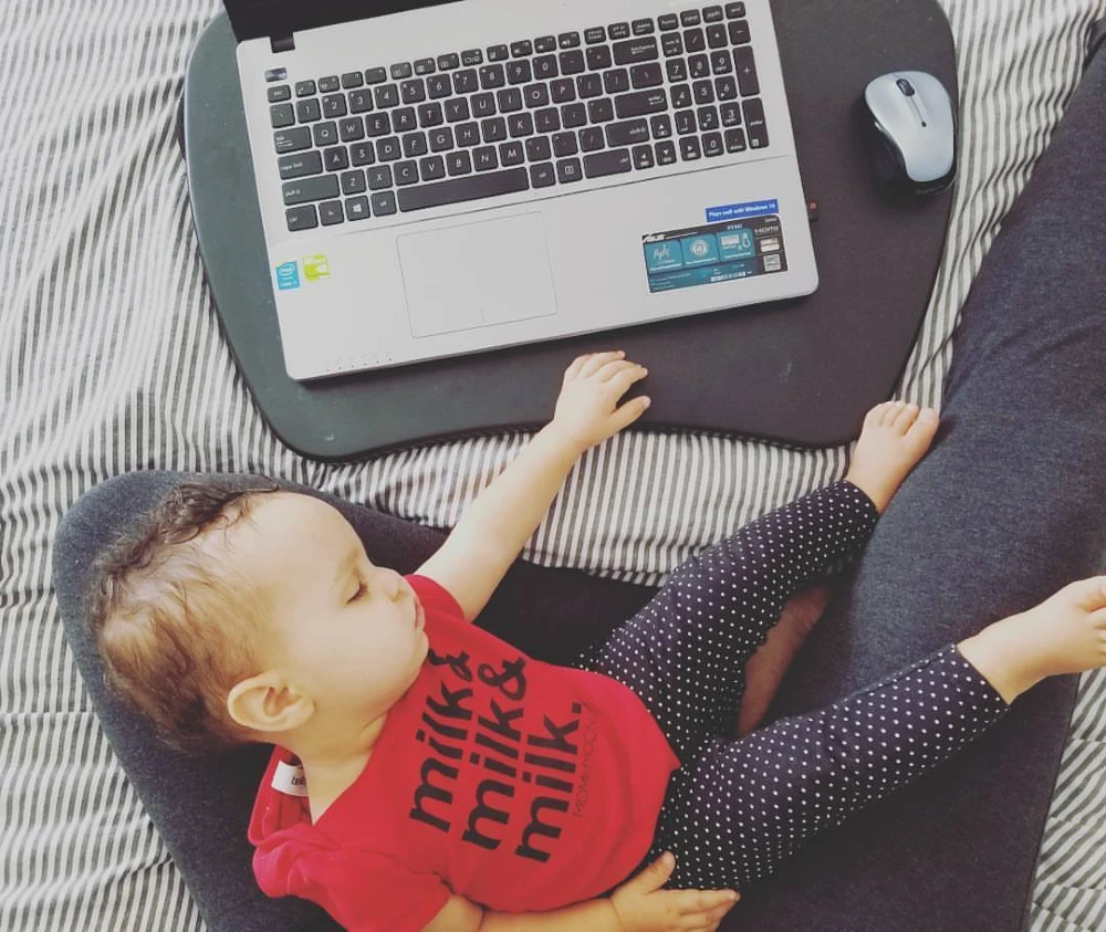 Baby sleeping on a parent’s lap next to an open laptop, showing the overlap of childcare and remote work