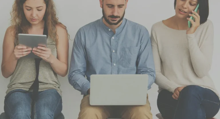 Three people sitting side-by-side working. The first person is on an ipad, the second is on a laptop and the third is making a call on a cellphone.